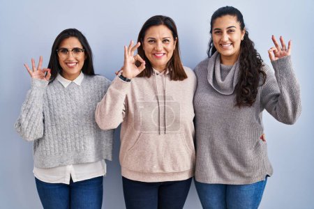 Photo for Mother and two daughters standing over blue background smiling positive doing ok sign with hand and fingers. successful expression. - Royalty Free Image