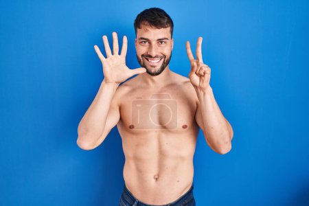 Téléchargez les photos : Handsome hispanic man standing shirtless showing and pointing up with fingers number seven while smiling confident and happy. - en image libre de droit