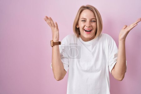 Téléchargez les photos : Young caucasian woman standing over pink background celebrating crazy and amazed for success with arms raised and open eyes screaming excited. winner concept - en image libre de droit