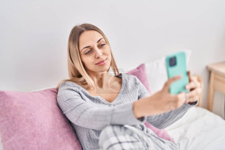 Photo for Young woman make selfie by the smartphone sitting on bed at bedroom - Royalty Free Image