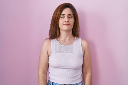 Photo for Brunette woman standing over pink background relaxed with serious expression on face. simple and natural looking at the camera. - Royalty Free Image