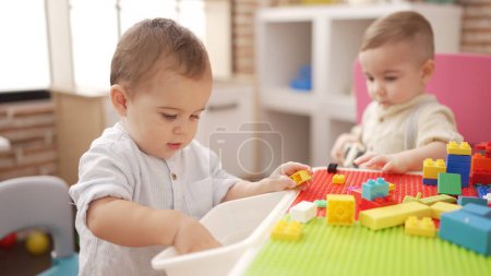 Téléchargez les photos : Deux adorables tout-petits jouant avec des blocs de construction assis sur la table à la maternelle - en image libre de droit