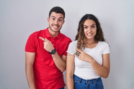Foto de Young hispanic couple standing over isolated background pointing aside worried and nervous with forefinger, concerned and surprised expression - Imagen libre de derechos