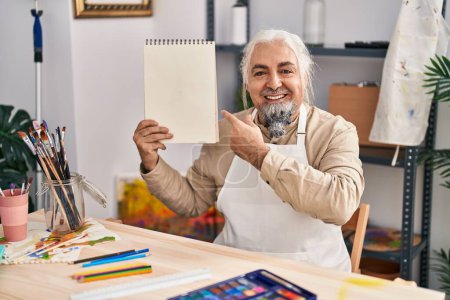 Photo for Middle age man with grey hair sitting at art studio holding notebook smiling happy pointing with hand and finger - Royalty Free Image