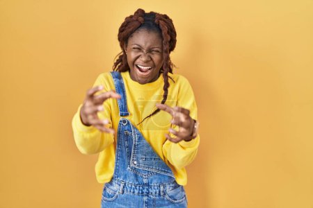 Photo for African woman standing over yellow background shouting frustrated with rage, hands trying to strangle, yelling mad - Royalty Free Image