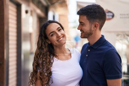 Foto de Joven pareja hispana sonriendo confiada abrazándose en la calle - Imagen libre de derechos