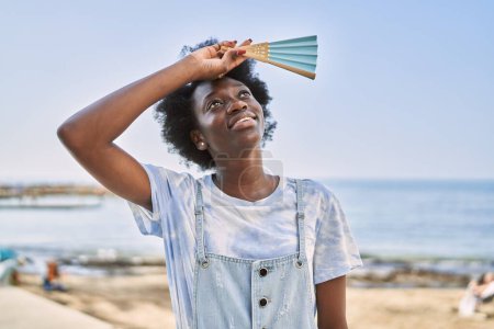 Foto de Mujer africana joven usando abanico de mano junto al mar - Imagen libre de derechos