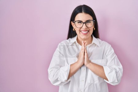 Photo for Young brunette woman standing over pink background praying with hands together asking for forgiveness smiling confident. - Royalty Free Image