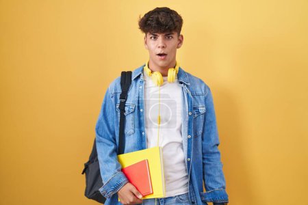 Foto de Adolescente hispana usando mochila de estudiante y sosteniendo libros en la cara de choque, mirando escéptico y sarcástico, sorprendido con la boca abierta - Imagen libre de derechos