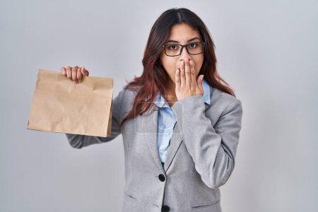 Photo for Hispanic young woman holding take away bag covering mouth with hand, shocked and afraid for mistake. surprised expression - Royalty Free Image