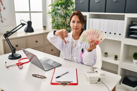 Photo for Hispanic doctor woman holding shekels banknotes at the clinic with angry face, negative sign showing dislike with thumbs down, rejection concept - Royalty Free Image