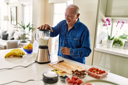 Foto de Hombre mayor sonriendo confiado batidor batidor en la cocina - Imagen libre de derechos