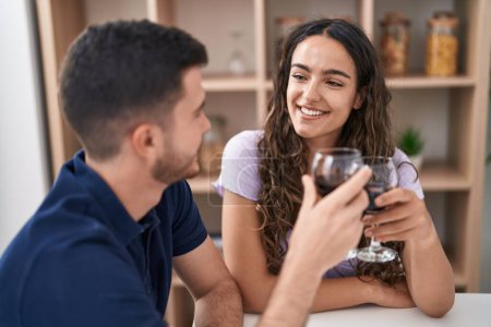Téléchargez les photos : Jeune couple hispanique buvant du vin assis sur la table à la maison - en image libre de droit