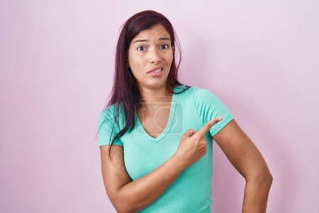 Téléchargez les photos : Jeune femme hispanique debout sur fond rose pointant de côté inquiet et nerveux avec index, expression inquiète et surprise - en image libre de droit