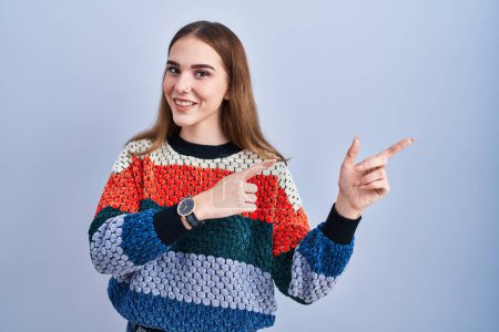 Photo for Young hispanic girl standing over blue background smiling and looking at the camera pointing with two hands and fingers to the side. - Royalty Free Image
