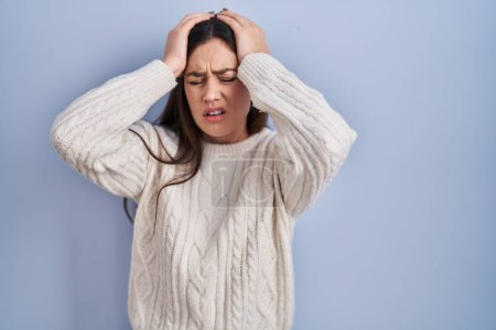 Photo for Young brunette woman standing over blue background suffering from headache desperate and stressed because pain and migraine. hands on head. - Royalty Free Image