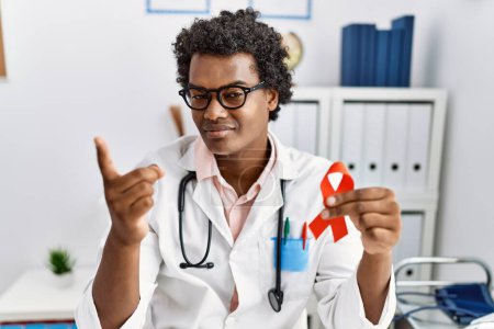 Photo for African doctor man holding support red ribbon smiling happy pointing with hand and finger to the side - Royalty Free Image