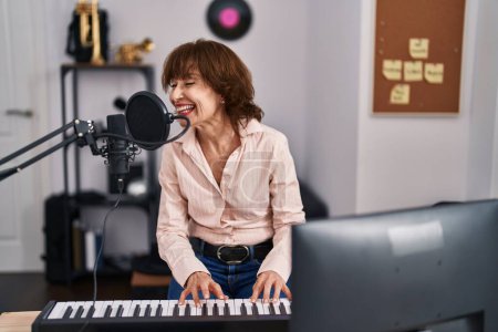 Téléchargez les photos : Middle age woman musician singing song playing piano at music studio - en image libre de droit