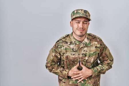 Foto de Joven hombre hispano usando uniforme camuflaje del ejército con la mano en el estómago porque las náuseas, la enfermedad dolorosa sensación de malestar. concepto ache. - Imagen libre de derechos