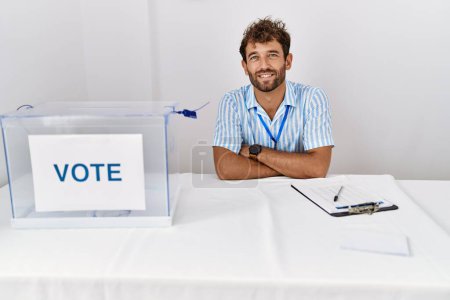 Téléchargez les photos : Jeune homme beau aux élections politiques assis par bulletin de vote visage heureux souriant avec les bras croisés regardant la caméra. personne positive. - en image libre de droit