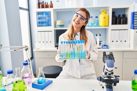 Photo for Young blonde woman wearing scientist uniform holding test tubes at laboratory - Royalty Free Image