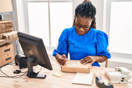 Photo for African american woman ecommerce business worker writing on package at office - Royalty Free Image