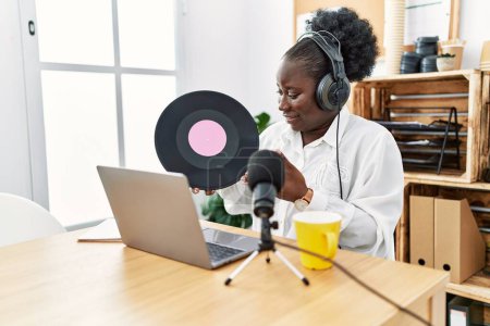 Téléchargez les photos : Jeune diffuseuse afro-américaine souriante confiante tenant un disque vinyle au studio de radio - en image libre de droit