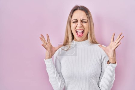 Photo for Young blonde woman wearing white sweater over pink background celebrating mad and crazy for success with arms raised and closed eyes screaming excited. winner concept - Royalty Free Image