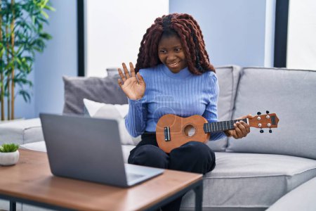 Photo for African woman playing ukulele at home doing video call looking positive and happy standing and smiling with a confident smile showing teeth - Royalty Free Image