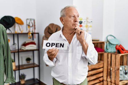 Photo for Senior man holding banner with open text at retail shop serious face thinking about question with hand on chin, thoughtful about confusing idea - Royalty Free Image