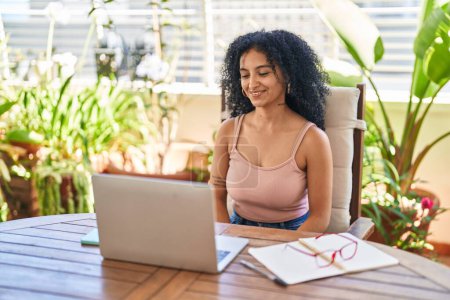 Photo for Young hispanic woman using laptop sitting on table at home terrace - Royalty Free Image