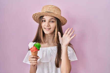 Téléchargez les photos : Adolescente tenant de la crème glacée renonçant à dire bonjour heureux et souriant, geste de bienvenue amical - en image libre de droit