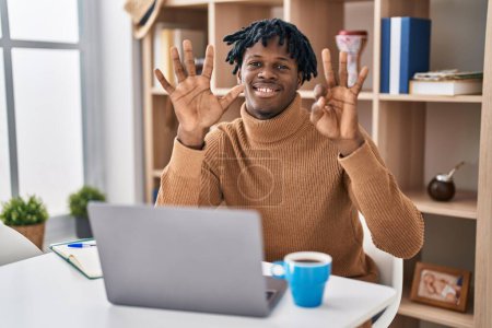 Foto de Young african man with dreadlocks working using computer laptop showing and pointing up with fingers number eight while smiling confident and happy. - Imagen libre de derechos