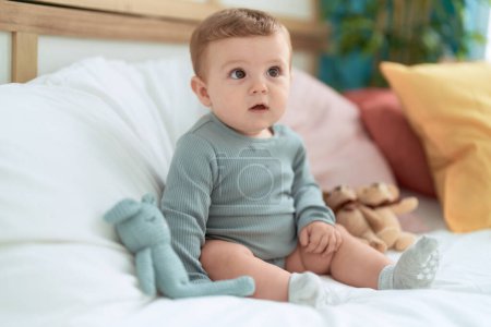 Foto de Adorable niño sentado en la cama con muñecas en el dormitorio - Imagen libre de derechos