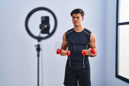 Photo for Hispanic man recording training tutorial at the gym skeptic and nervous, frowning upset because of problem. negative person. - Royalty Free Image
