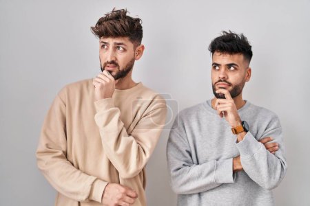 Foto de Young homosexual couple standing over white background thinking worried about a question, concerned and nervous with hand on chin - Imagen libre de derechos