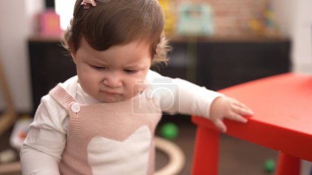 Foto de Adorable niño de pie con expresión relajada apoyado en la mesa en el jardín de infantes - Imagen libre de derechos