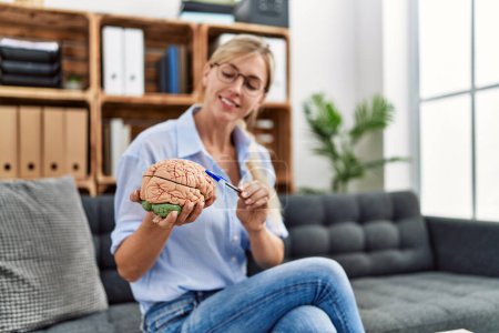 Photo for Young blonde woman psychologist holding brain sitting on sofa at clinic - Royalty Free Image