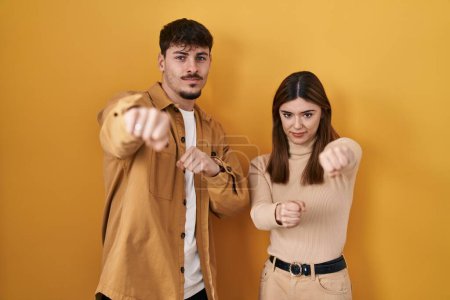 Photo for Young hispanic couple standing over yellow background punching fist to fight, aggressive and angry attack, threat and violence - Royalty Free Image