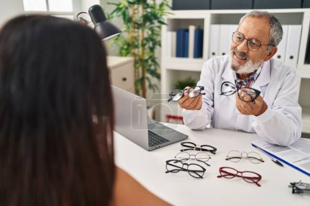 Photo for Senior grey-haired man optician holding glasses showing to patient at clinic - Royalty Free Image
