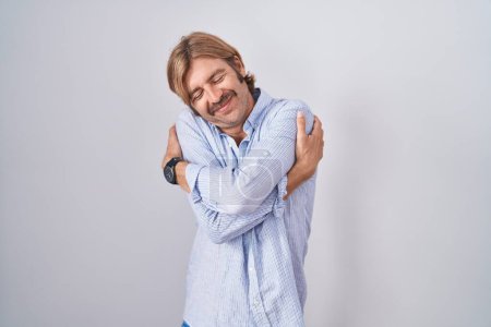 Photo for Caucasian man with mustache standing over white background hugging oneself happy and positive, smiling confident. self love and self care - Royalty Free Image