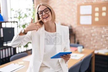 Téléchargez les photos : Young caucasian woman working at the office wearing glasses smiling cheerful showing and pointing with fingers teeth and mouth. dental health concept. - en image libre de droit
