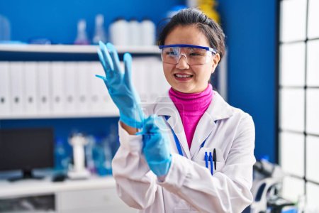 Foto de Joven científica china sonriendo confiada usando guantes en el laboratorio - Imagen libre de derechos