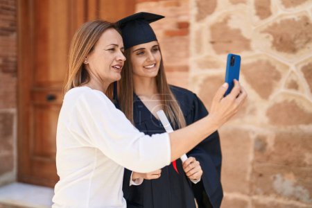 Photo for Two women mother and graduated daughter making selfie by smartphone at campus university - Royalty Free Image
