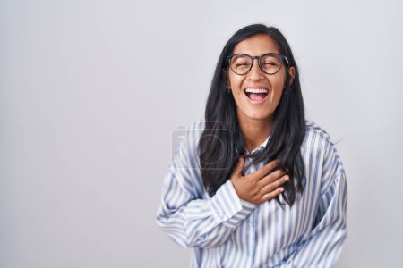 Téléchargez les photos : Jeune femme hispanique portant des lunettes souriant et riant fort à haute voix parce que drôle blague folle avec les mains sur le corps. - en image libre de droit