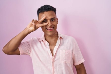 Téléchargez les photos : Jeune homme hispanique debout sur fond rose faisant symbole de paix avec les doigts sur le visage, souriant joyeux montrant la victoire - en image libre de droit