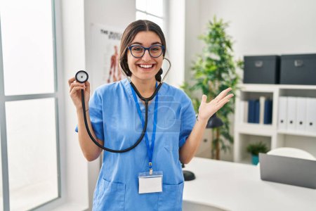 Photo for Young hispanic doctor woman wearing stethoscope at the clinic celebrating victory with happy smile and winner expression with raised hands - Royalty Free Image