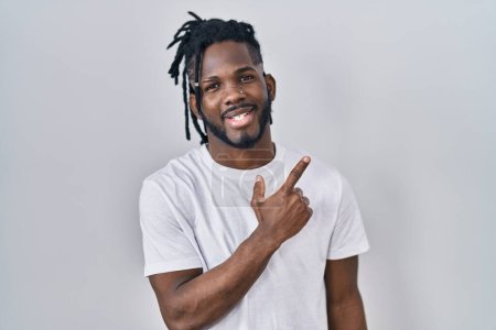 Photo for African man with dreadlocks wearing casual t shirt over white background cheerful with a smile of face pointing with hand and finger up to the side with happy and natural expression on face - Royalty Free Image