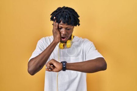Téléchargez les photos : Young african man with dreadlocks standing over yellow background looking at the watch time worried, afraid of getting late - en image libre de droit