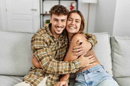 Photo for Young hispanic couple smiling happy and hugging sitting on the sofa at home. - Royalty Free Image